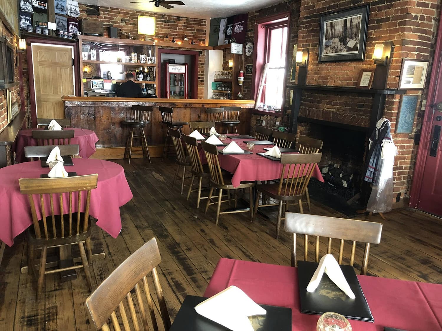 Cozy restaurant interior featuring wooden tables with red tablecloths and a fireplace.