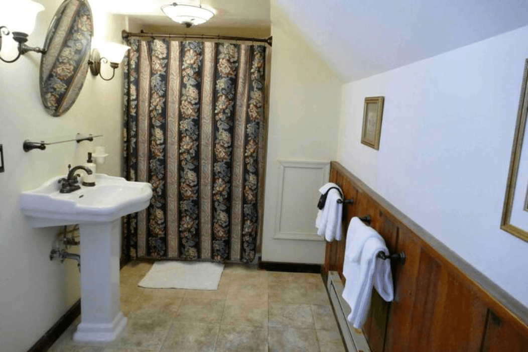 A vintage-style bathroom with a sink, a floral shower curtain, and neatly hung white towels.
