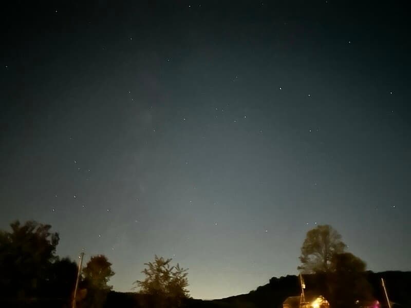 A clear night sky filled with stars, above a dark landscape.