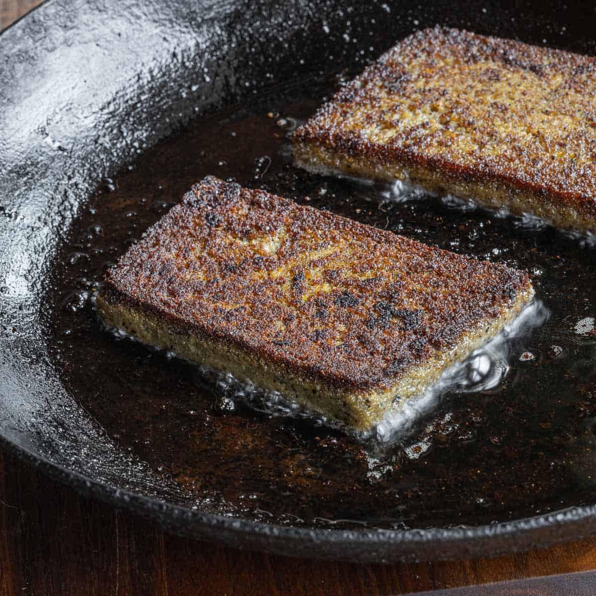 Two golden-brown rectangles frying in a dark cast-iron skillet.