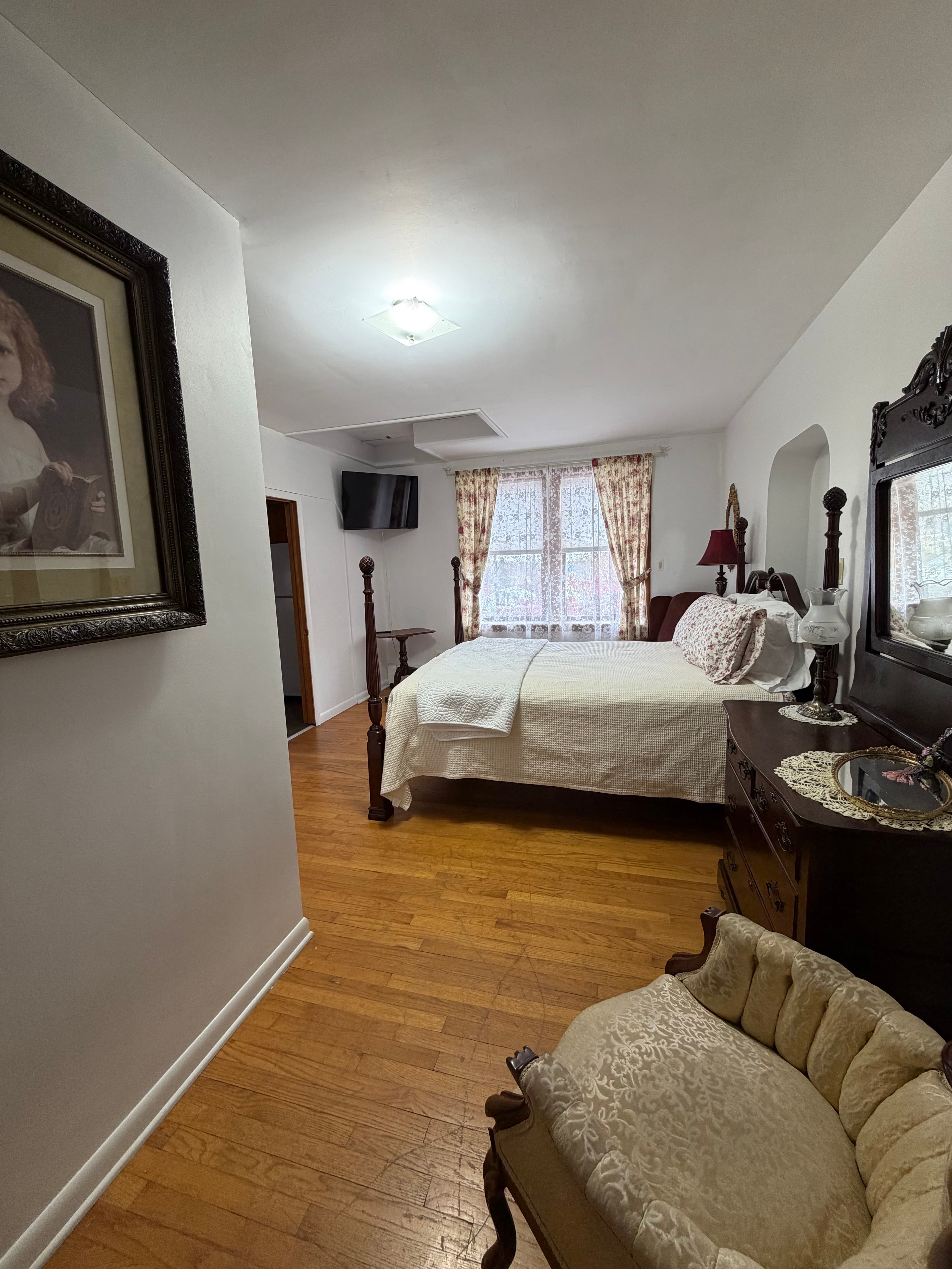 Cozy bedroom featuring a bed, antique furniture, and large windows with curtains.