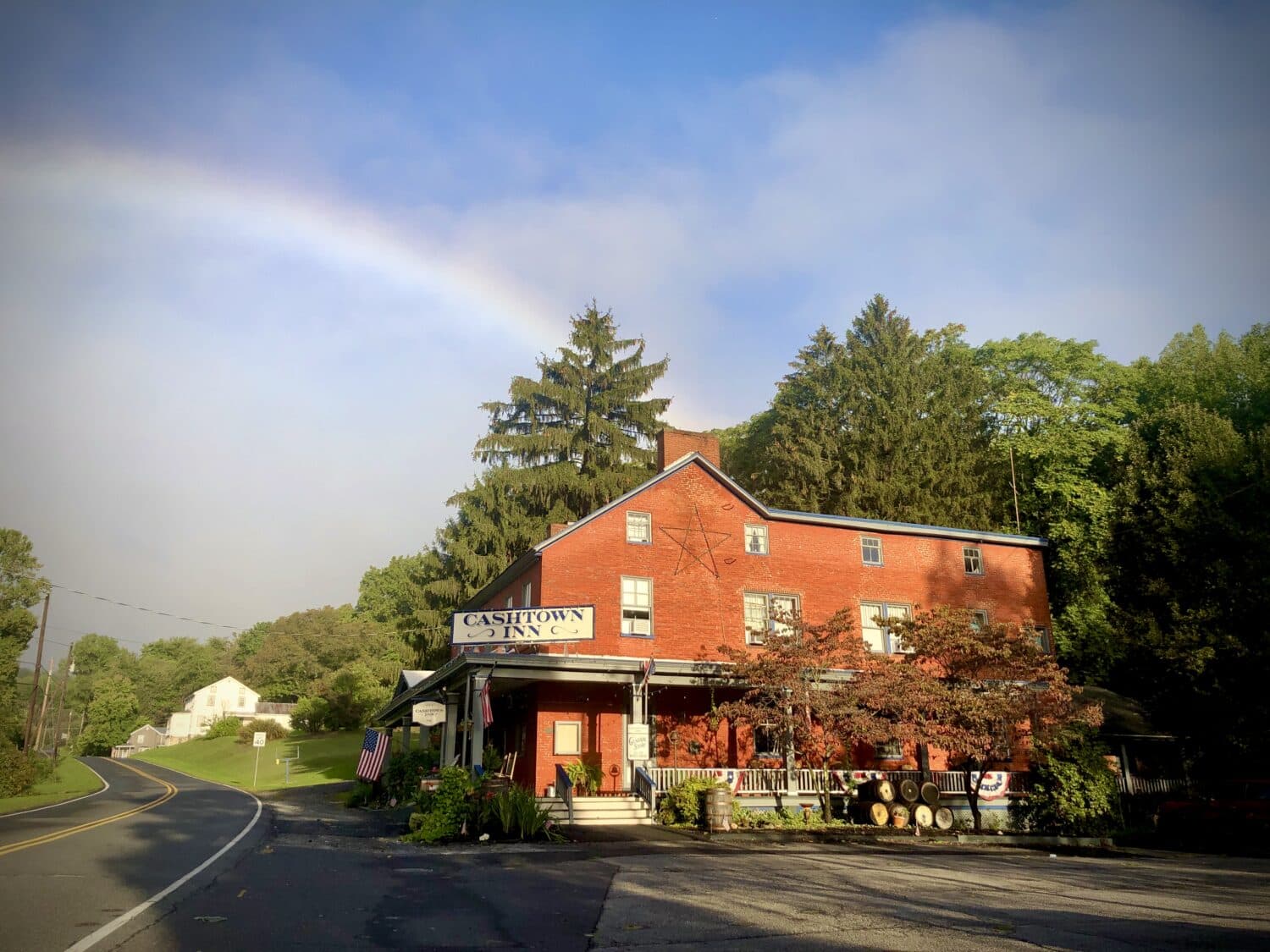 A red building labeled "Cashtown Inn" is situated beside a winding road, under a rainbow and surrounded by trees.