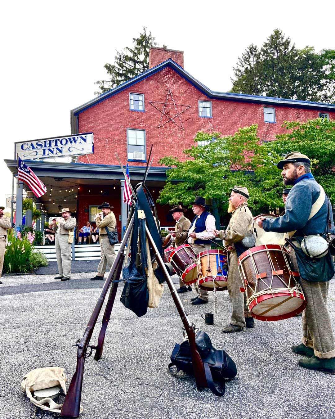 A group of historical reenactors in military attire plays drums in front of the Cashtown Inn.