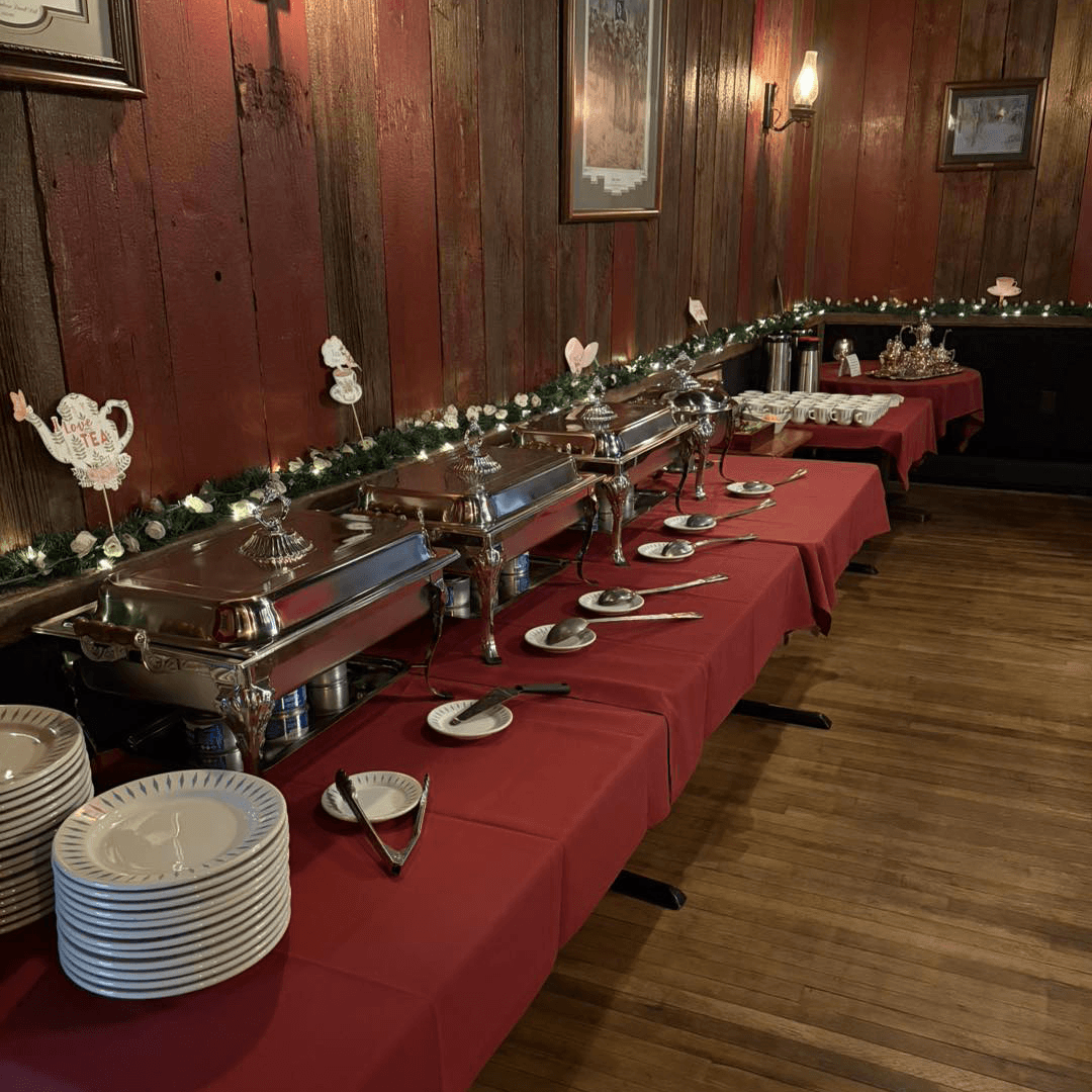 A buffet setup with silver chafing dishes on red tablecloths, surrounded by white plates and festive decorations.