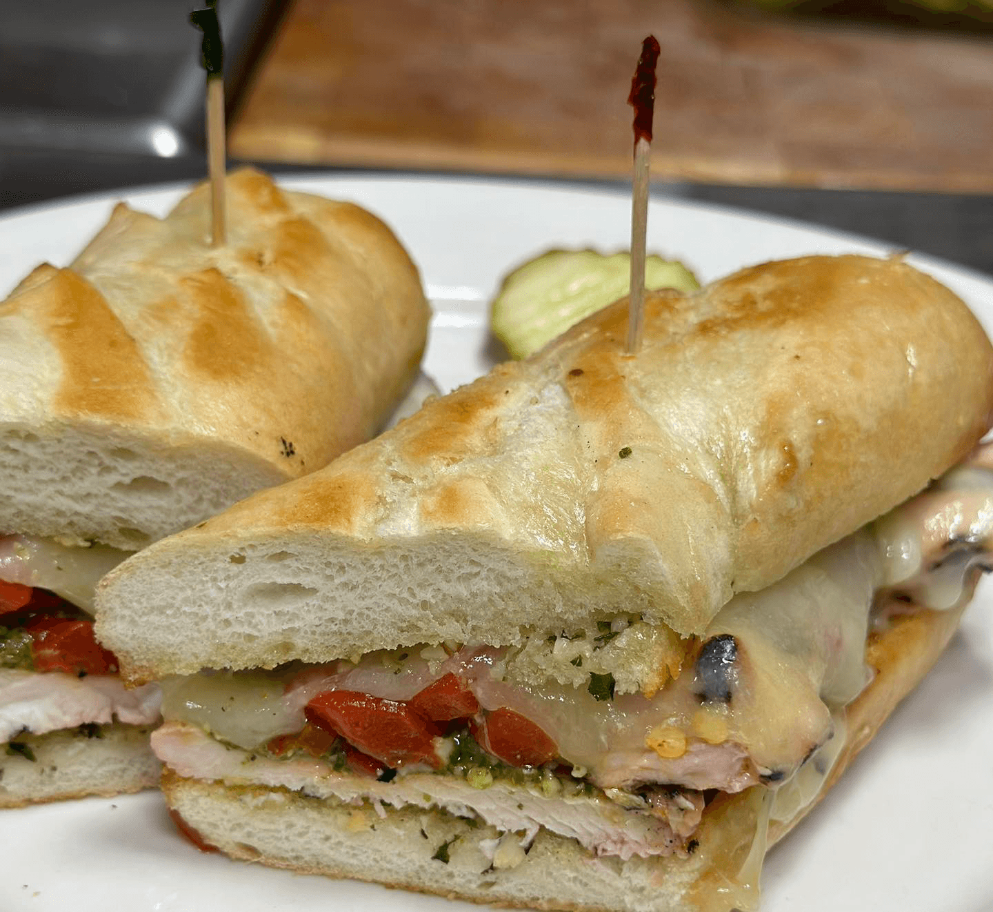 A freshly cut sandwich filled with turkey, cheese, and vegetables, garnished with pickles.