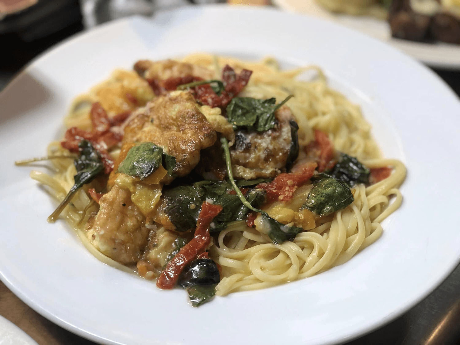 A plate of spaghetti topped with chicken, spinach, sun-dried tomatoes, and melted cheese.