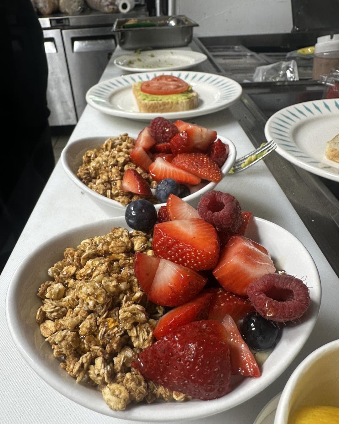 Three bowls filled with granola, mixed berries, and a plate with a slice of toast topped with tomato.