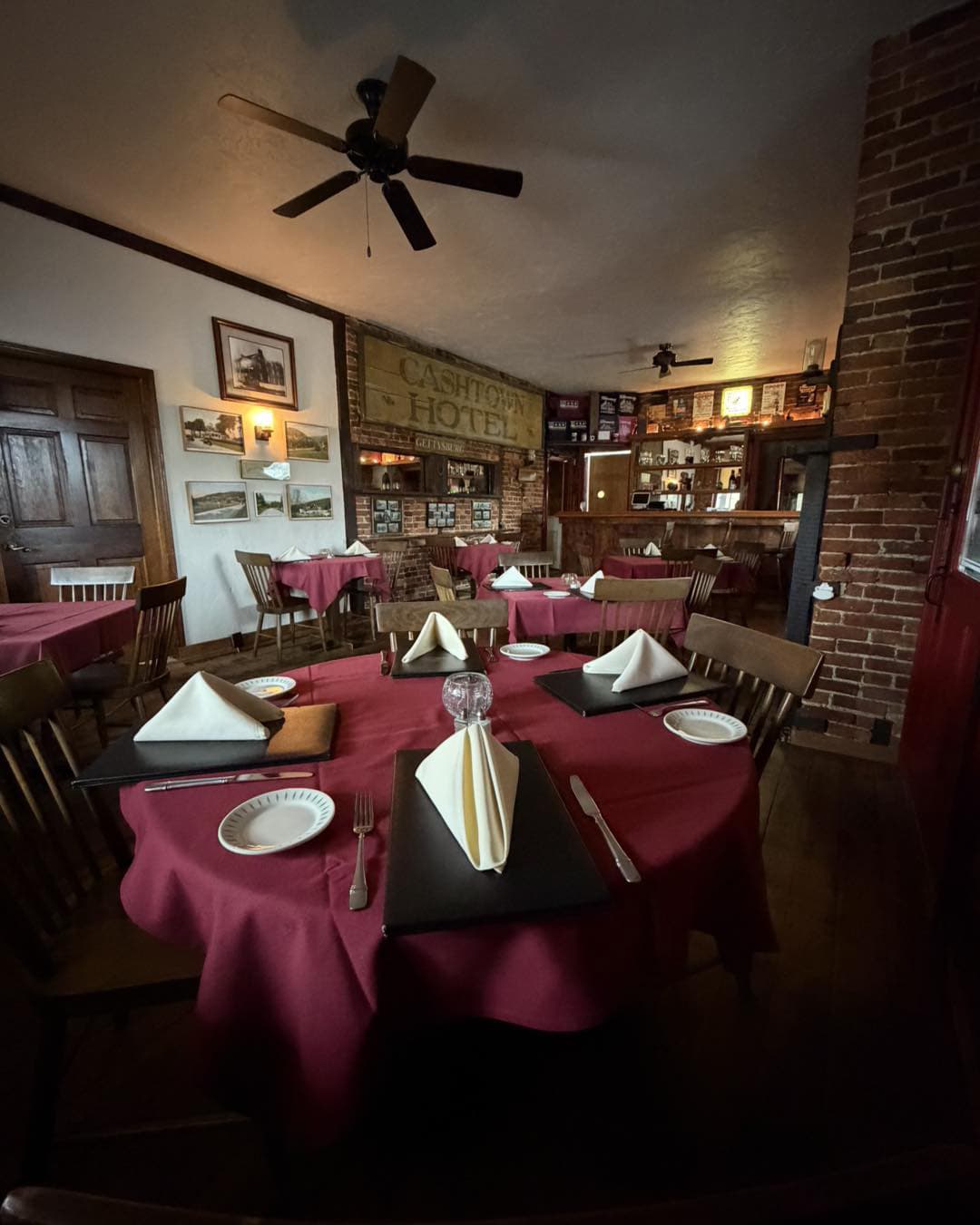A cozy dining room with wooden tables set with red tablecloths, napkins, and menus against a backdrop of brick walls and vintage decor.